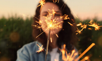 A young woman holds a sparkler in her hands, selective focus. Celebrates the holiday outside, new...