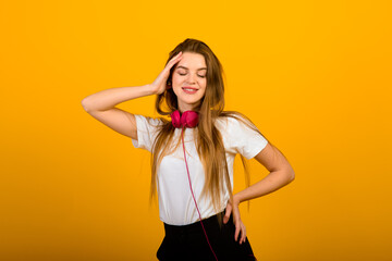 Isolated portrait of happy woman has toothy smile, closes eyes, feels pleasure from compliment, stands over yellow wall. Positive emotions and feelings concept