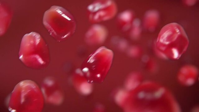 Juicy grains of ripe pomegranate are falling on the red background in slow motion