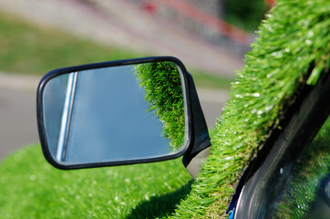 Car mirror with green artificial grass around. Reflection of sky. Zero emissions vehicle concept