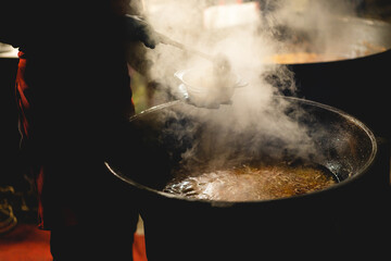 cook scoops up food from a cauldron