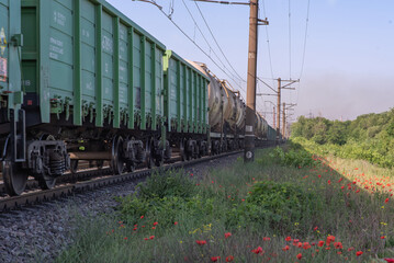 Fototapeta na wymiar Freight train movement on the railway paths along blooming poppies.