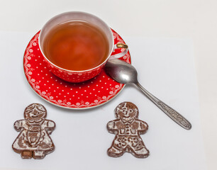 Red Cup with black tea and saucer with a metal teaspoon and ginger biscuits in the form of men on a...