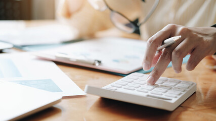 Fototapeta premium Close up Businesswoman using calculator and laptop for do math finance on wooden desk in office and business working background, tax, accounting, statistics and analytic research concept