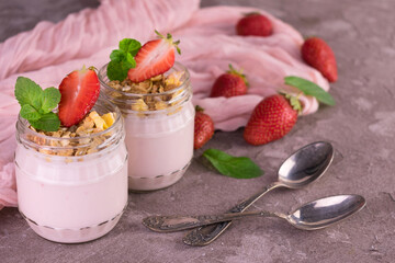 Two jars of strawberry yogurt on a gray background.