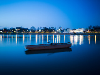 Naklejka premium Blue hour on Sava river, promenade in Slavonski Brod and blurred boat in front.