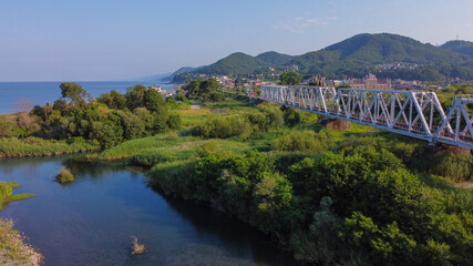 Fototapeta premium Aerial view of the railway bridge running along the sea coast. The confluence of the Shakhe river with the Black sea. Golovinka, Sochi, Russia.