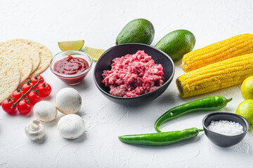 Raw ingredients for tacos with minced beef meat, corn tortillas, chili, avocado, over white background. Side view.