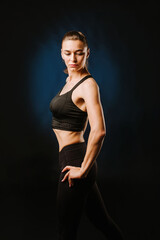 Fototapeta premium Slim fitness woman in black sport suit posing on black background