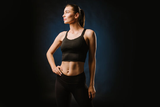 Slim fitness woman in black sport suit posing on black background