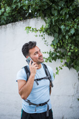 Young man with backpack and light blue shirt talking on the phone on the street