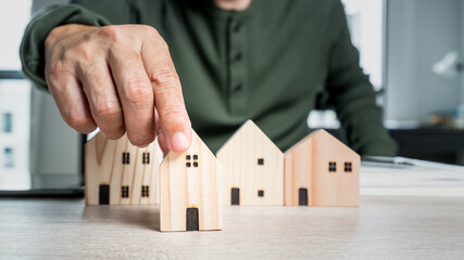 Man hand select a home model on the wood table. Loan or saving money to buy a new house in the future concept.