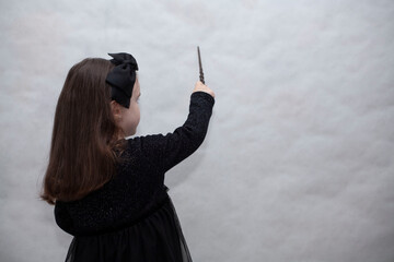 Little girl in a black dress shows a pointer on a white background. There is a place for text