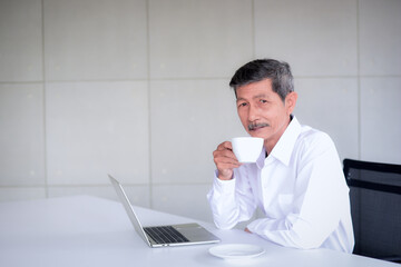 Asian Elderly aging or Retirement age have adapted to the world of technology Can use IT equipment To work and communicate online In the relaxed work room while sipping coffee in a good mood