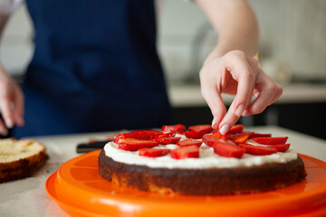 Obraz na płótnie Canvas young woman decorates a birthday cake with strawberries. cake decoration.
