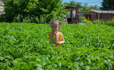 A little girl in a yellow dress is standing in the garden. Palm rested against chin. Happy child.