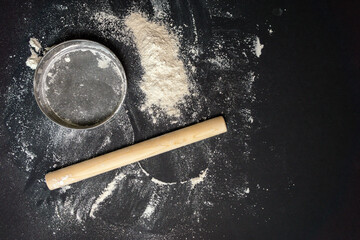 flour, sieve rolling pin for making bread on a black background top view flat lay