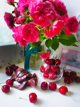 On the table a bouquet of beautiful roses with cherries in a glass