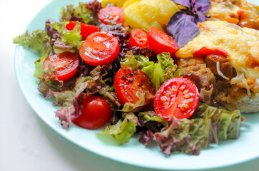 Prepared meat dish with potato slices and cherry tomatoes with salad