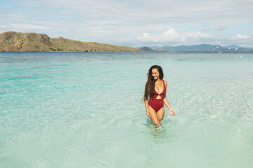 Young slim beautiful woman having fun and splashing water on beach with amazing transparent turquoise water. Leisure and relaxation. Wanderlust travel and vacations.