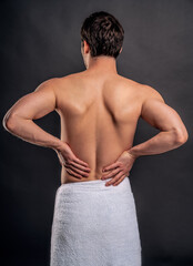Handsome young bearded man isolated. Portrait of topless muscular man is standing on gray background. Man holding his back. Experiencing backache.