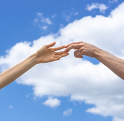 Male and female hand reach for each other and touch their fingers on a background of blue sky and white clouds. Lending a helping hand. Solidarity, compassion,and charity, rescue. Volunteer concept.