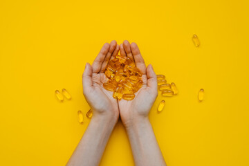 Female hands holding a bunch of fish oil capsules on bright yellow background.
