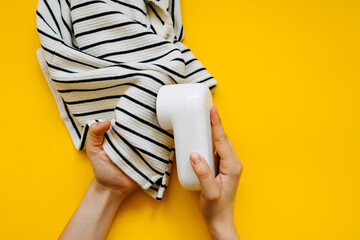 Female hands holding a spool remover machine removing spools from a cloth, on bright yellow background.