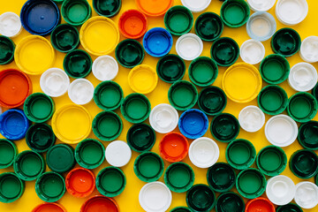 Lots of colorful plastic bottle caps on a bright yellow background. Concept of global warming and garbage.