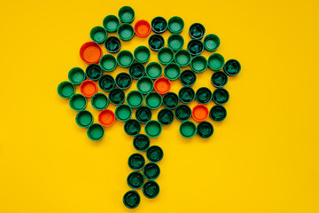 Green plastic caps in shape of a tree on clean background. Concept of pollution and recycling.