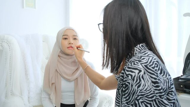 Muslim woman wearing hijab head scarfs and make up artist applying lipstick to her mouth.