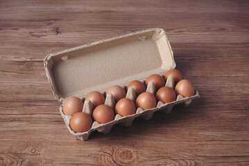 Raw chicken eggs in cardboard box on brown wooden background.