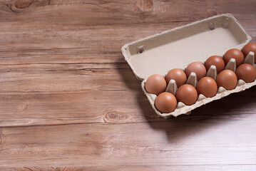 Raw chicken eggs in cardboard box on brown wooden background with copy space.
