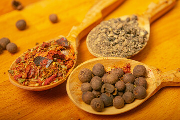 Black allspice, coarse salt and various ground spices in wooden spoons on a wooden Board. Close up.