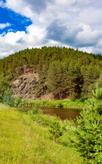 Summer landscape with trees, rocks and river against blue sky with clouds