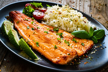 Fried salmon steak with rice and vegetables on wooden table

