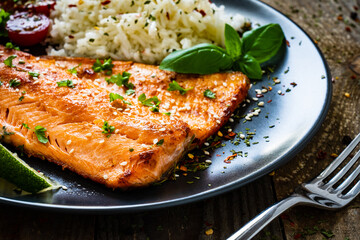 Fried salmon steak with rice and vegetables on wooden table
