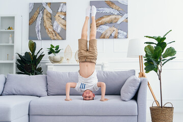 Adorable child standing on his head on sofa at home stock photo