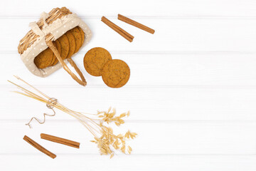 Oatmeal cookies with oat stems ears and cinnamon sticks on white wood table. Top view, flat lay. Food autumn background in rustic style