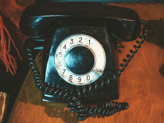 Closeup photo of an old black dial telephone on a wooden table