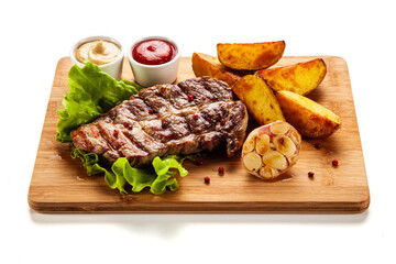 Grilled steak with baked potatoes and vegetables served on wooden board on white background