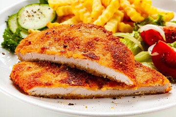Breaded fried pork chop, French fries and vegetables on white background
