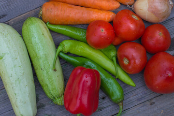 A variety of fresh vegetables, tomatoes, onions, zucchini, carrots, red and green peppers, on a rustic wooden table.