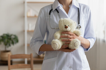 Crop close up of female medical specialist or nurse in white uniform hold stuffed teddy bear in...