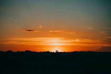 Orange sunset with silhouettes of trees in the evening. Clouds over the contours of forest