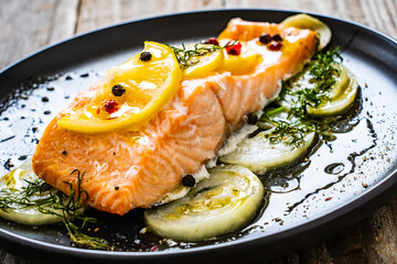 Roasted salmon steak with lemon, and onion served on black plate on wooden table
