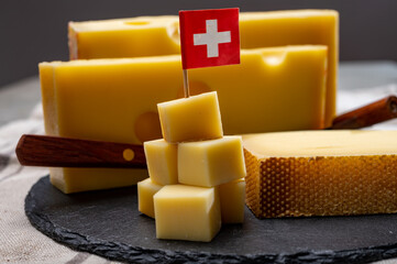 Swiss cheeses, block of medium-hard yellow cheese emmental or emmentaler with round holes and matured gruyere served in cubes as mountain top with Swiss flag.