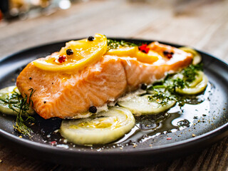 Roasted salmon steak with lemon, and onion served on black plate on wooden table