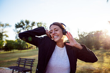 Happy cheerful woman with smile on face listening music on headphones outdoor