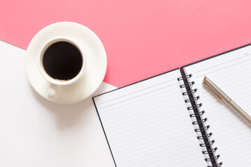 Flat lay of coffee, blank notebook and pen on split color pink and white background. Business concepts